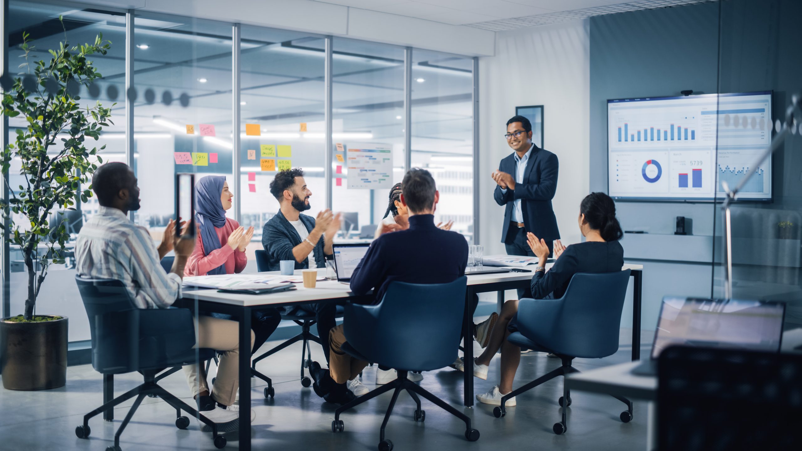 Multi-Ethnic Office Conference Room. Indian CEO does Presentation for Diverse Young Entrepreneurs, Talking, Using TV with Infographics, Statistics, Graphs. Businesspeople Invest in e-Commerce Startup